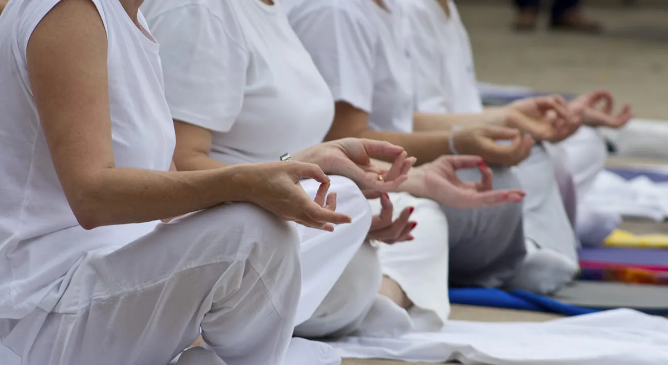 Orang-orang duduk bersama dalam meditasi dengan tangan bertumpu di lutut